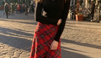 Woman in a red tartan wrap skirt with a black fitted top, black tights and ankle boots on a festive cobbled street