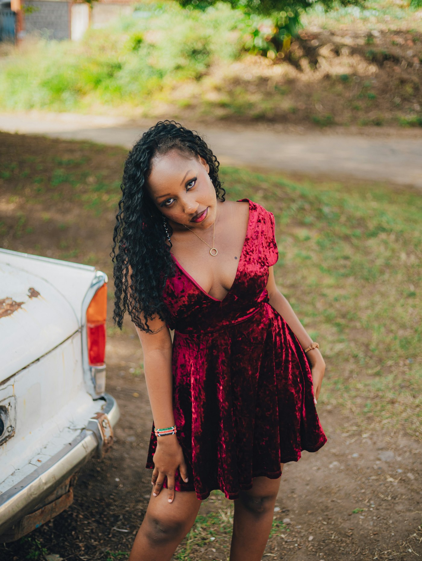 Woman in a red velvet dress posing by an old car, a velvet winter wedding guest idea