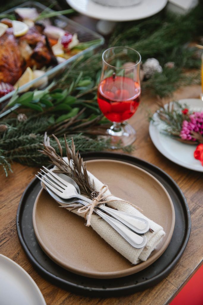 Linen napkin and silverware tied with twine and a rosemary sprig on a stoneware plate at a rustic table