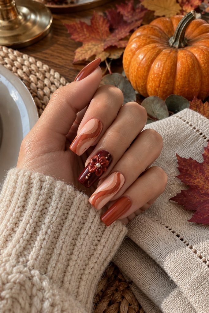 Long square nails in peach and terracotta swirls with a burgundy nail, a raised red flower and small pearls