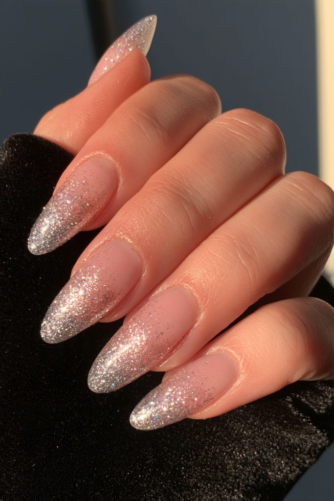 Hand with silver glitter ombre almond nails resting on black velvet