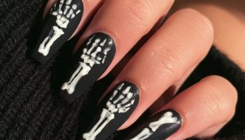 Hand with long coffin nails in black with white skeleton bone art resting on a black sweater