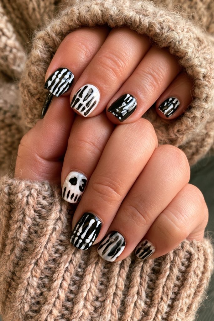Two hands with matching black and white skeleton nails and a skull accent nail in cozy knit sleeves