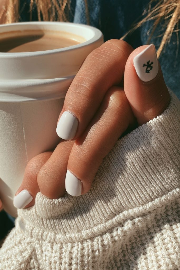 Hand with short milky white nails and a small black skull accent holding a coffee cup