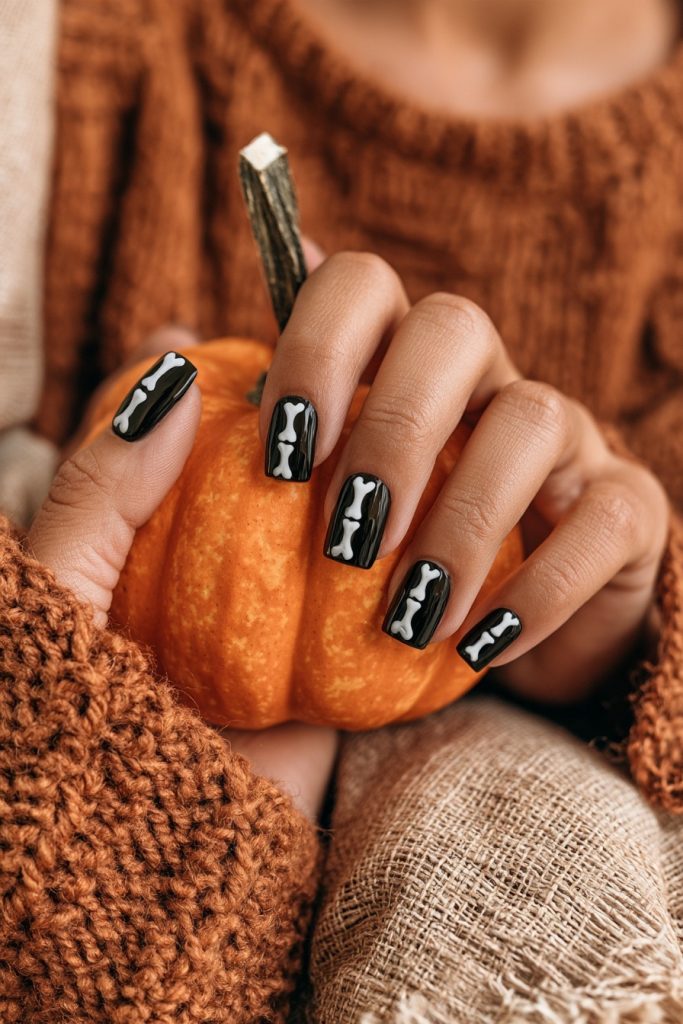 Hand with short square black nails and white bone lines holding a small pumpkin