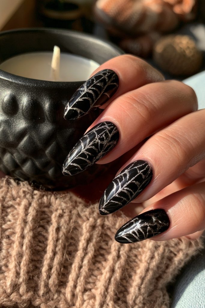 Hand with long almond black nails and silver spider web lines beside a black candle holder