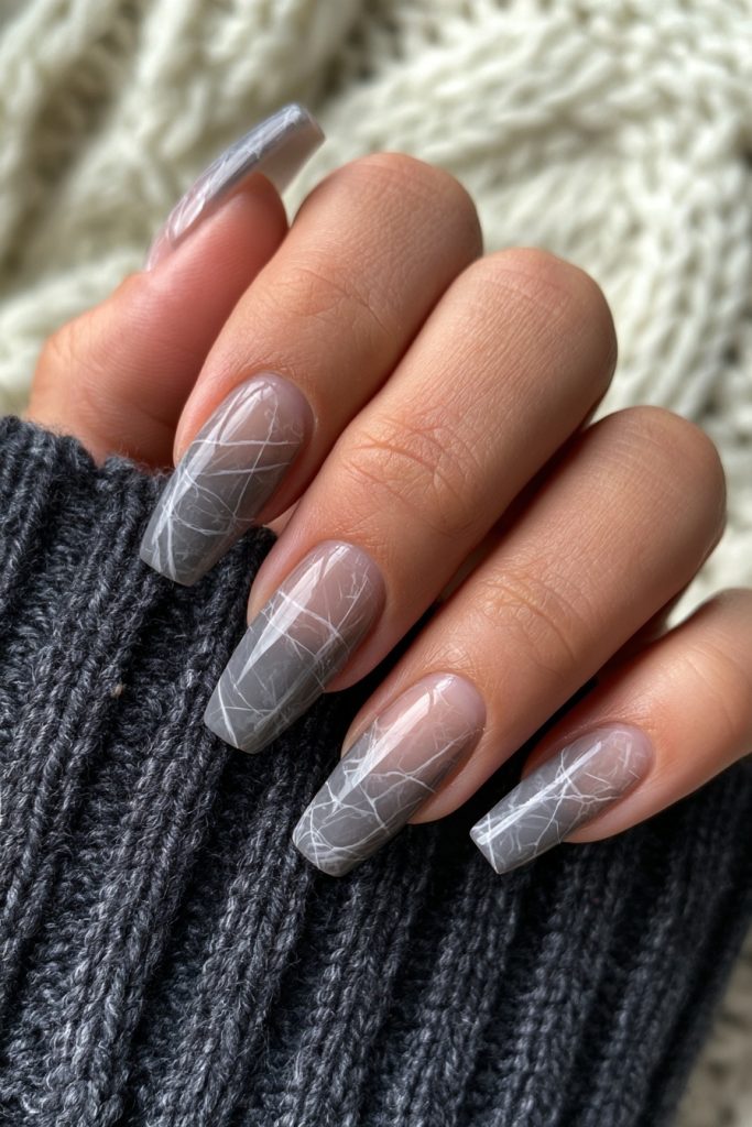 Hand with coffin nails in sheer smoky grey with white spider web lines resting on a dark knit sweater
