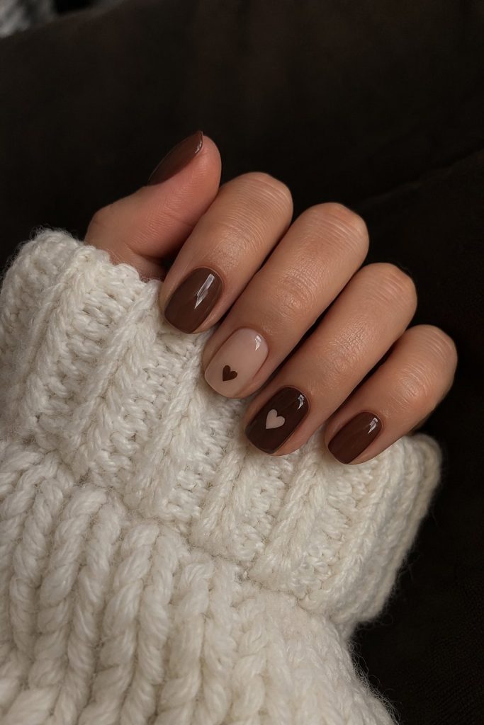 Glossy chocolate brown nails and a nude accent nail with tiny painted hearts