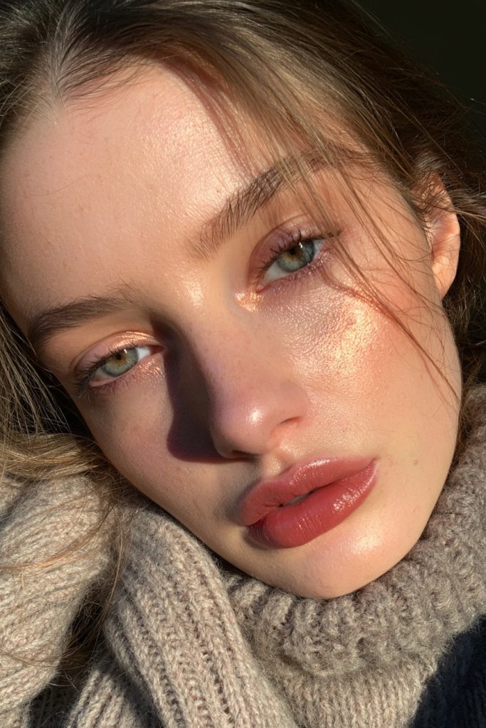 Woman with a berry stained lip and glowing skin with copper highlighter wearing a knit collar