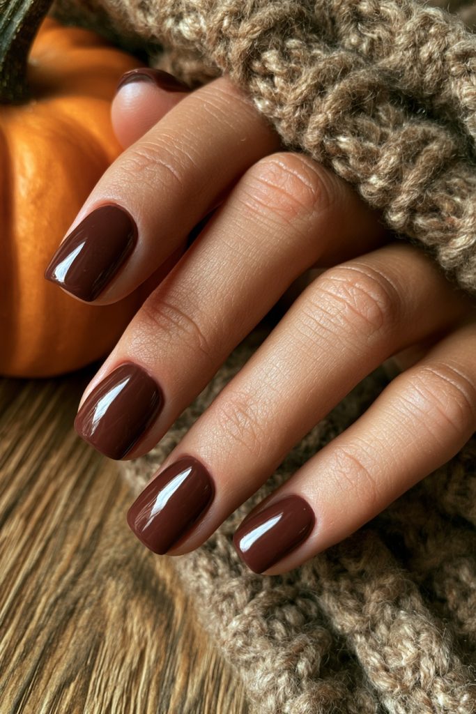 Hand with short glossy chocolate brown nails resting against a chunky knit sleeve