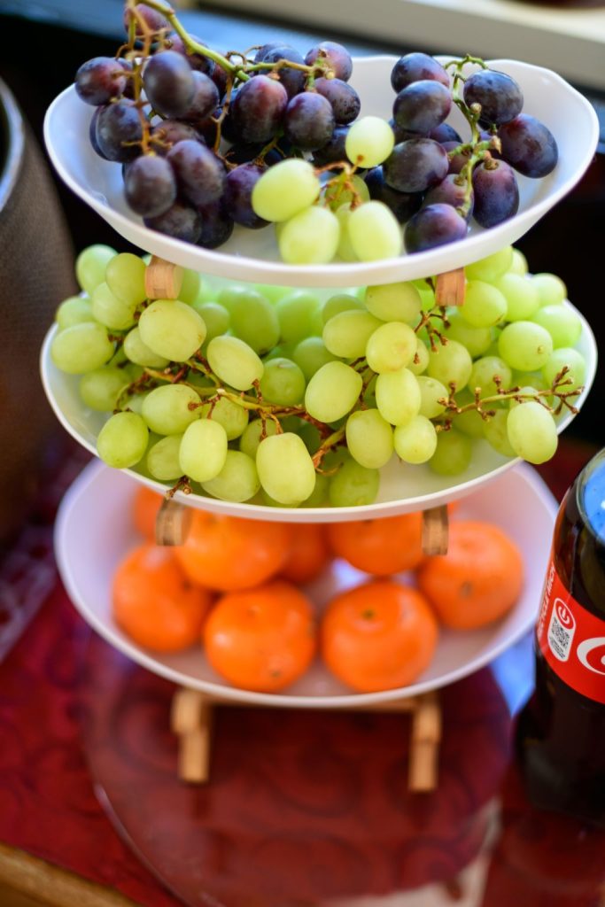 Three tiered white fruit stand piled with red grapes, green grapes and mandarin oranges