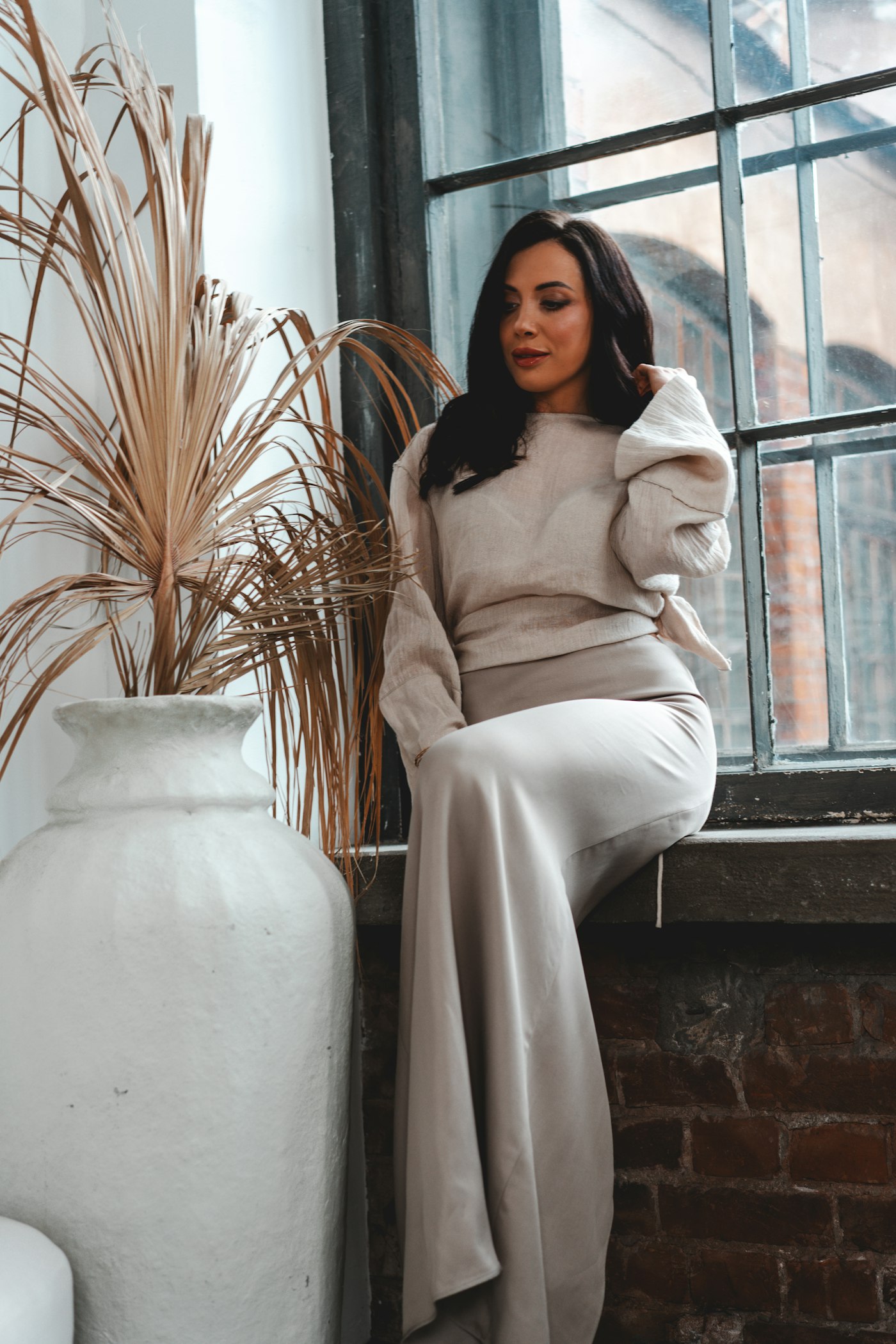 Woman in a neutral outfit sitting by a window