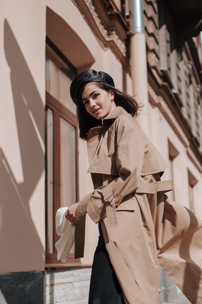 Woman in a belted camel trench coat and a black beret turning with the coat flowing out behind her