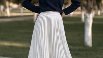 Woman in a navy turtleneck with a white pleated midi skirt and tan suede ankle boots in a park
