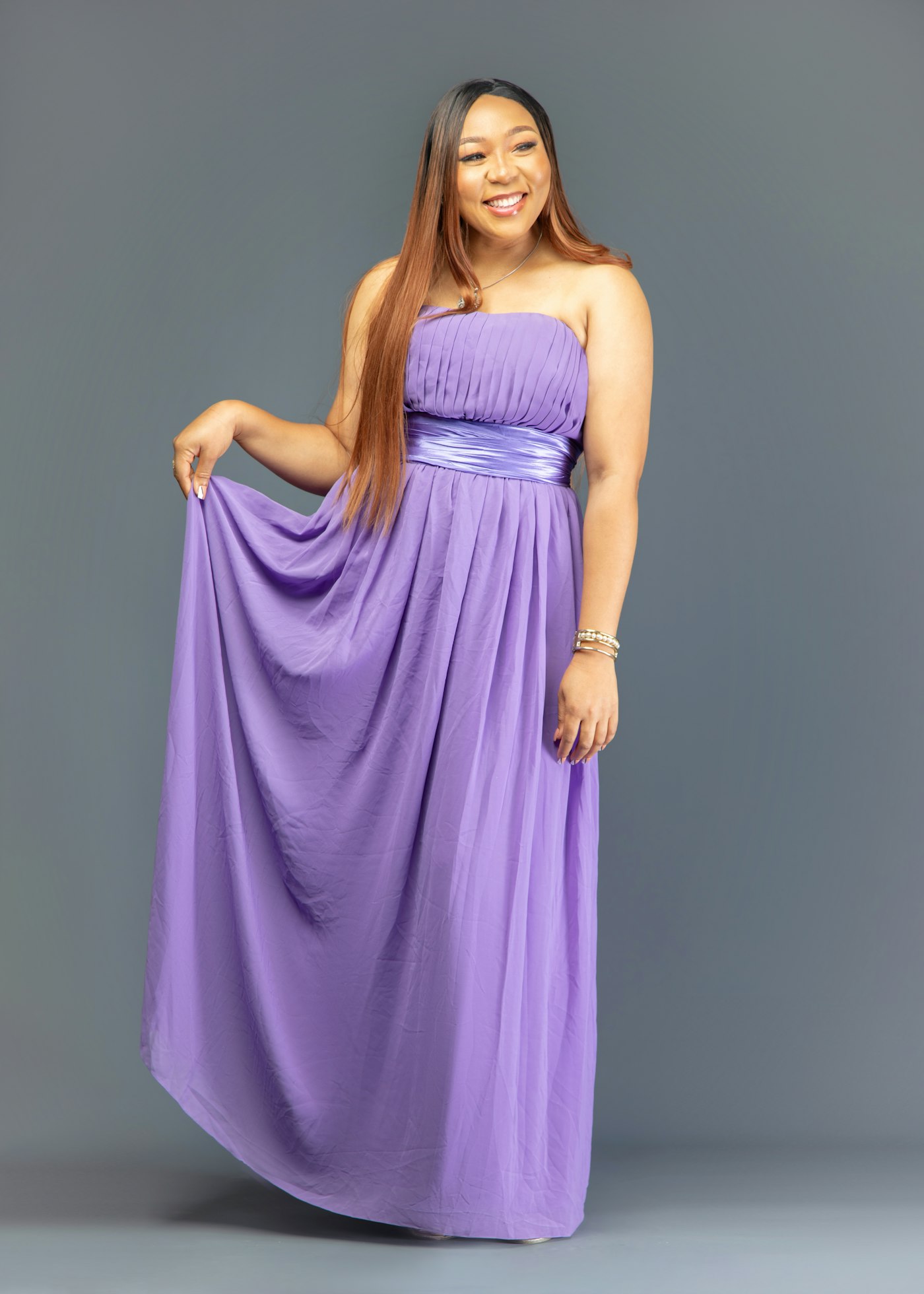 Woman in a strapless purple gown holding the skirt against a grey background