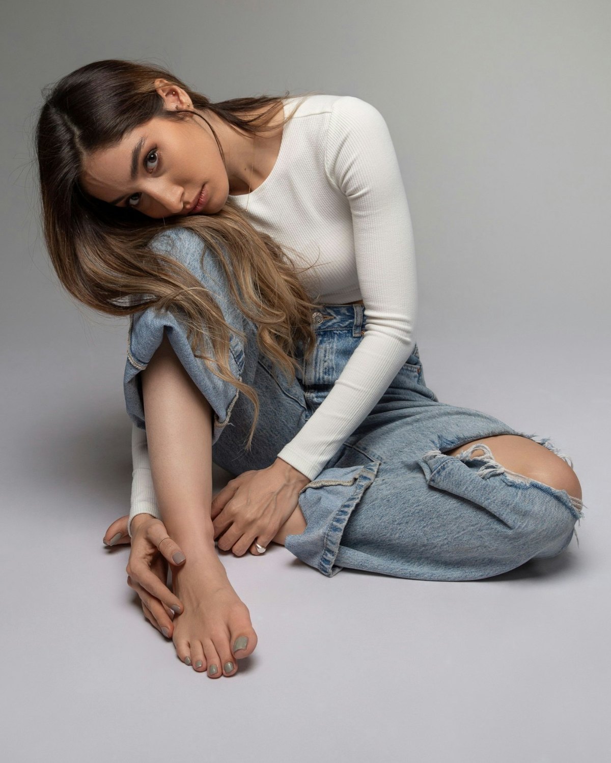 Woman in a white long-sleeved shirt and jeans sitting on the floor