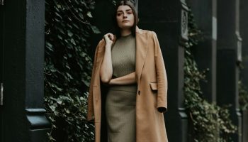 Woman in a brown coat standing near a black metal gate