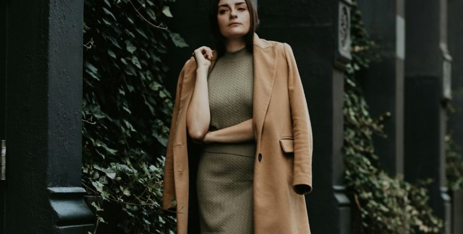 Woman in a brown coat standing near a black metal gate