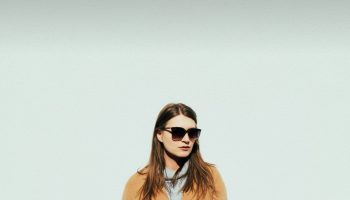 Woman in a tan wool coat and sunglasses on a winter day